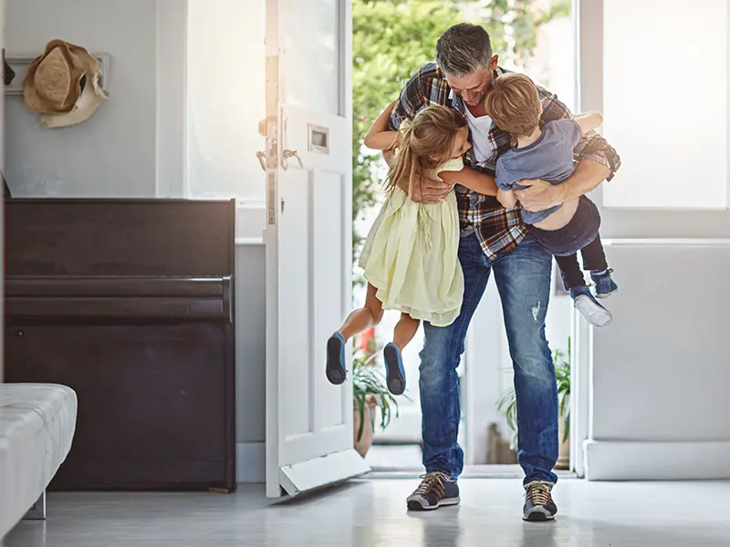 A father hugging his son and daughter together in a doorway at home