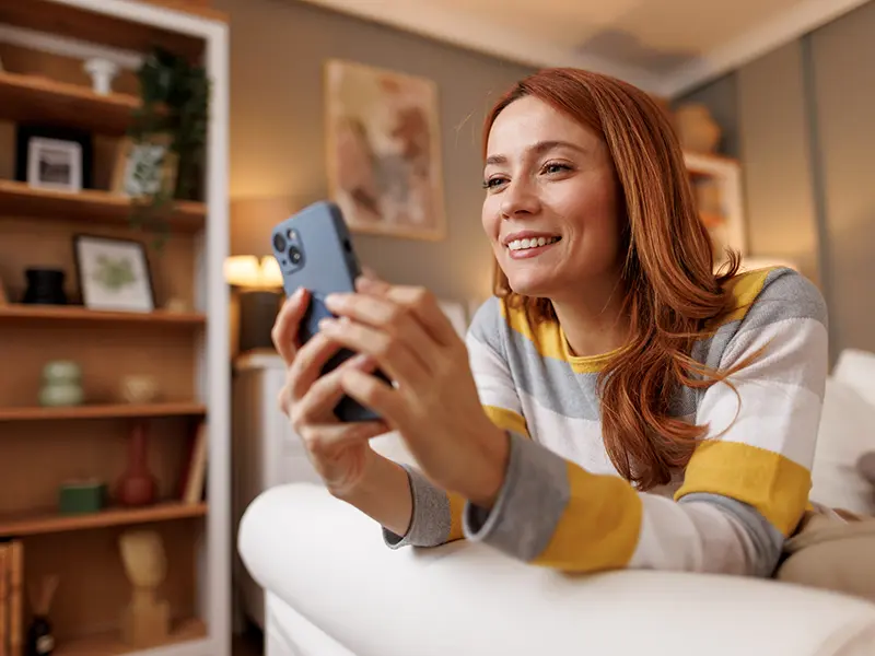 Smiling young woman lying down using smartphone