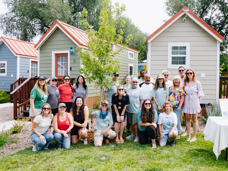 Large group posing on lawn in front of small cottages and trees