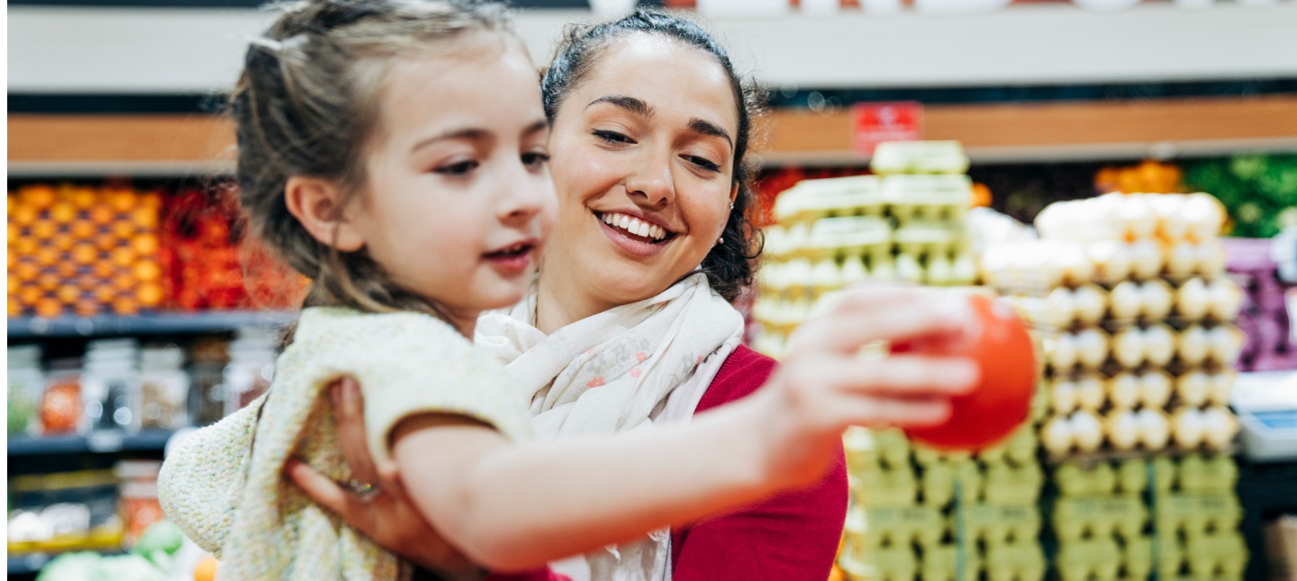 Mother and daughter at grocery store picking produce.