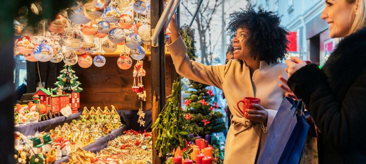 Smiling woman shopping for holiday ornaments at outdoor holiday market.