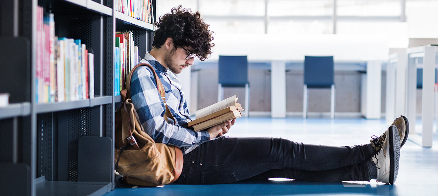 Young male student reading a book in a library.
